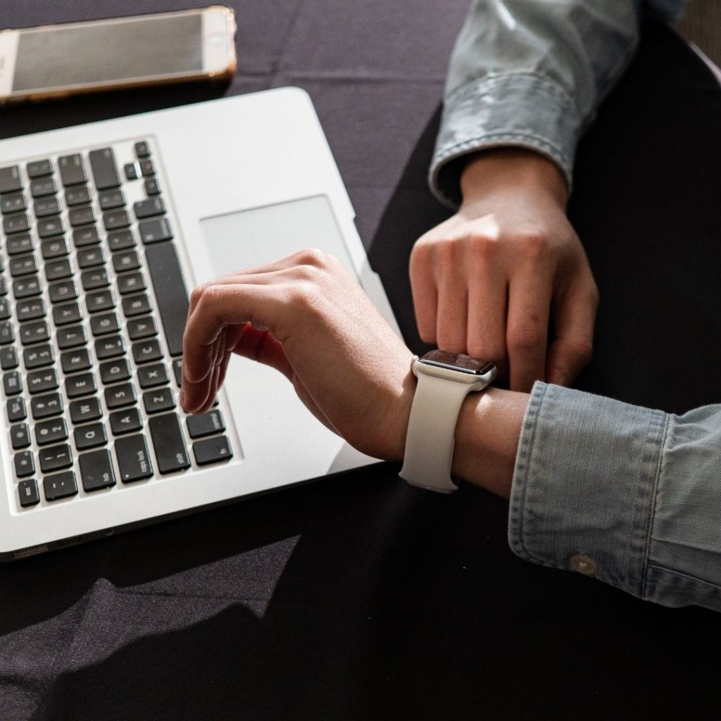 Seroang pria menggunakan jam tangan sedang bekerja di depan laptop