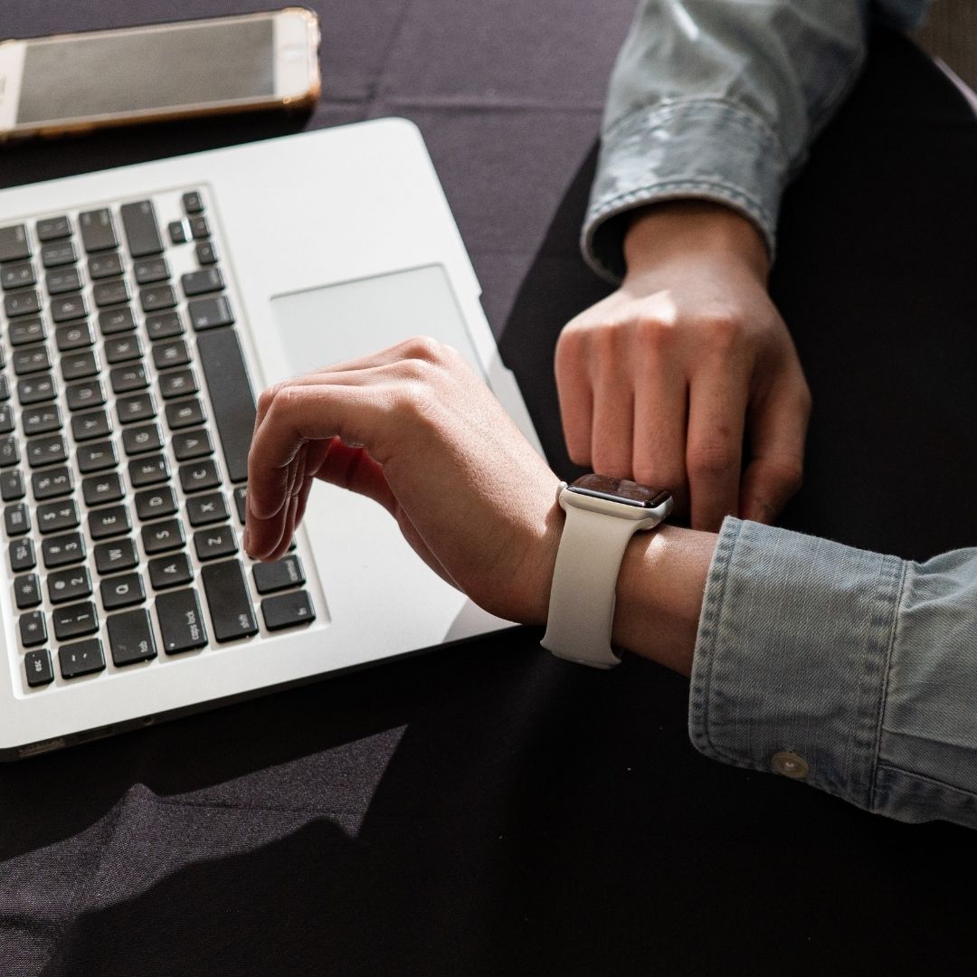 Seroang pria menggunakan jam tangan sedang bekerja di depan laptop